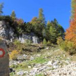 Rdeče-bela planinska markacija ob poti med skalami in jesenskim drevjem