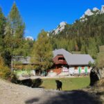 Planinski dom na Zelenici med travniki in jesensko obarvanimi macesni